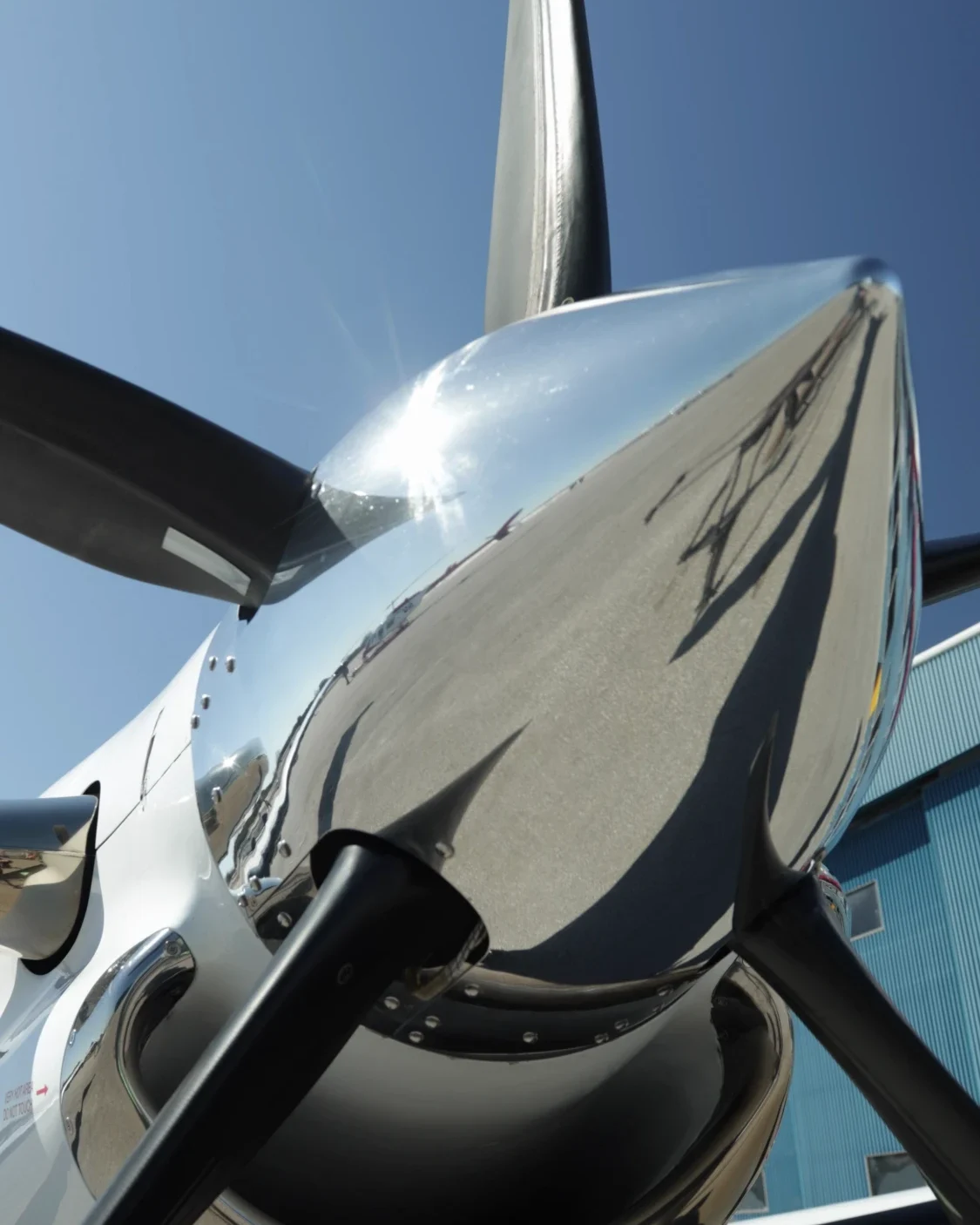 The polished spinner and propeller blades of a NectAir turboprop, against a blue sky