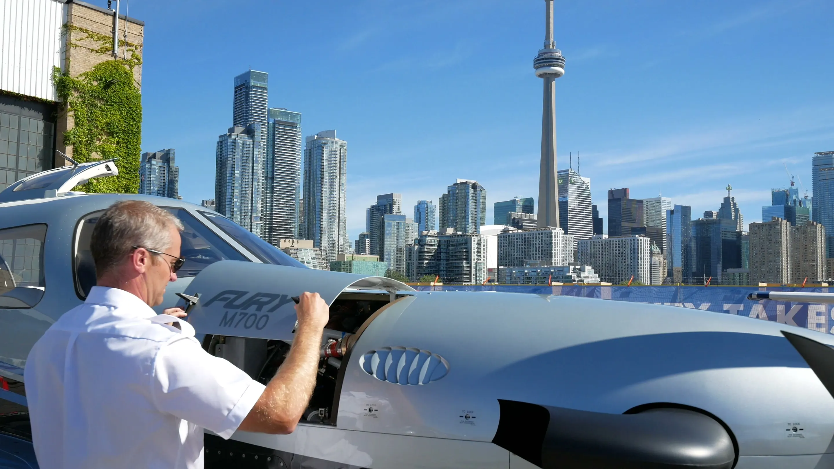 A NectAir pilot latching the engine cowling of our Piper M700 before flight, Toronto behind